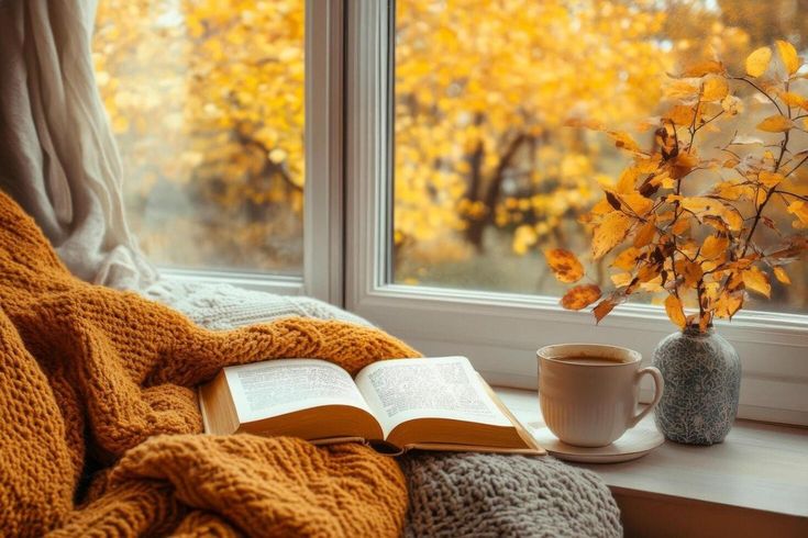 Tavolo con libro e tisana davanti a finestra con panorama autunnale